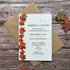 A plantable wedding invitation card with a vertical border of orange and red autumn leaves, placed on top of a brown kraft envelope on a rustic wood background with scattered fall leaves.