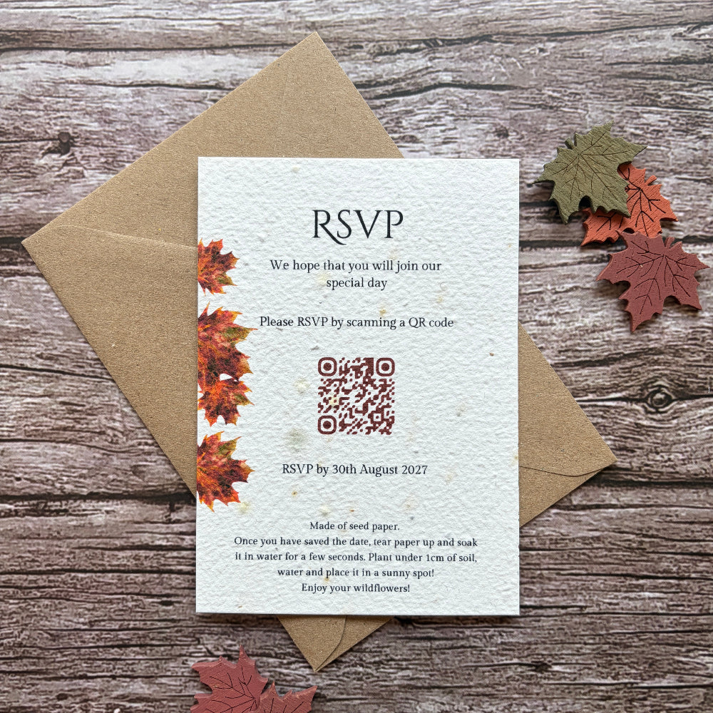 A handmade plantable wedding reception invitation card with autumn maple leaf illustrations, placed on top of a brown kraft envelope on a rustic wooden background with decorative fall leaves.