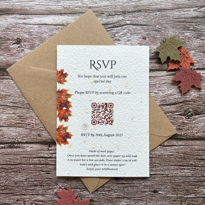 A handmade plantable wedding reception invitation card with autumn maple leaf illustrations, placed on top of a brown kraft envelope on a rustic wooden background with decorative fall leaves.