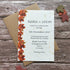 Plantable autumn wedding invitation card with a vertical border of orange and red autumn leaves on the left, placed on top of a kraft paper envelope on a rustic wood surface. Small decorative leaves are scattered around it.