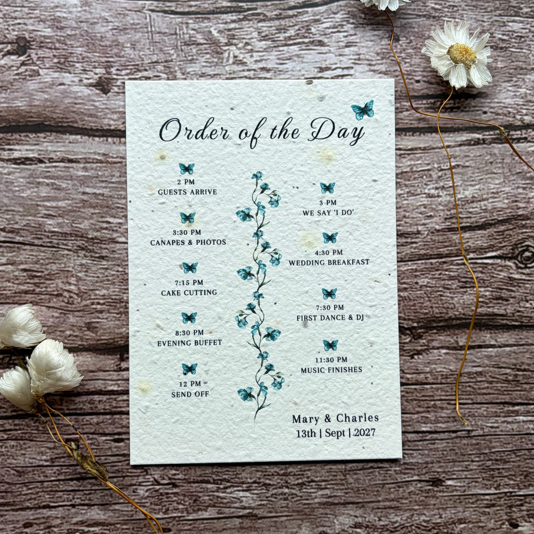 Order of the Day card on a wooden surface with flowers with blue sweet peas printed on seed paper