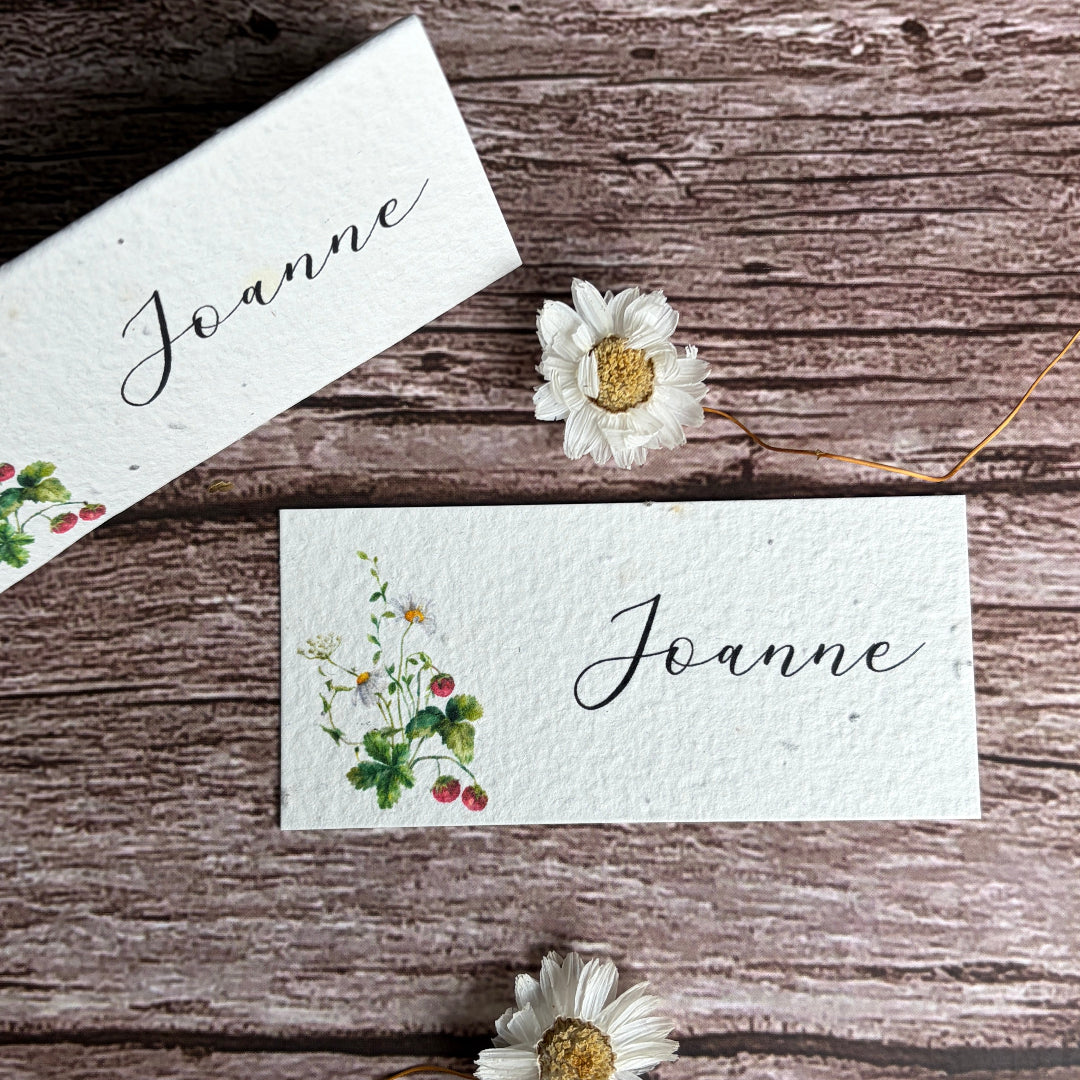 plantable name cards with strawberries and wildflowers designs on a wooden surface