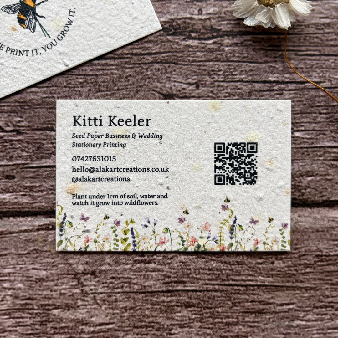 Seed paper business card with floral design and QR code on a wooden surface with a flower.