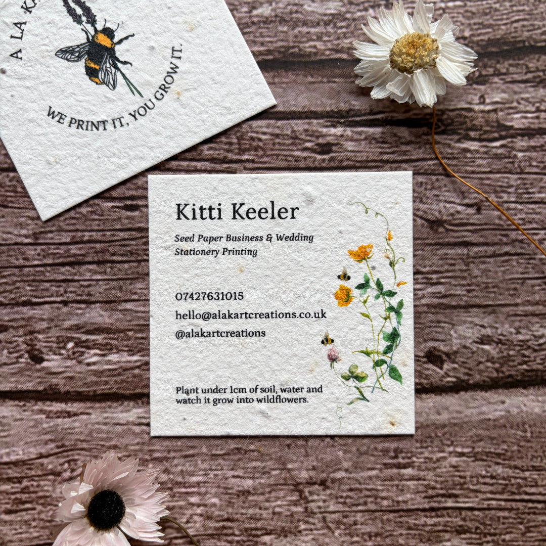 Seed paper square business card with floral design on a wooden surface with flowers around