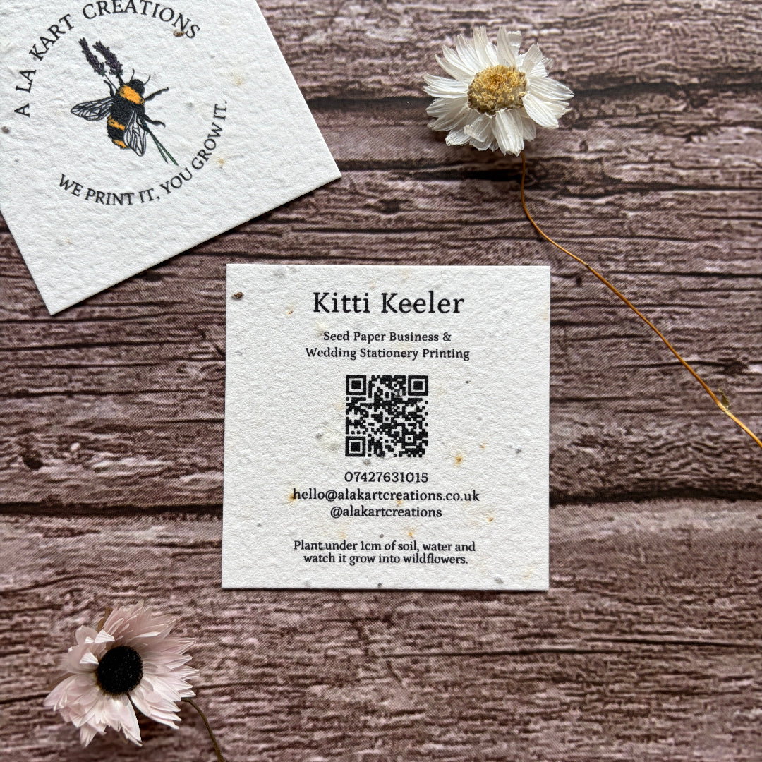 Plantable square business cards with bee design on a wooden surface with flowers