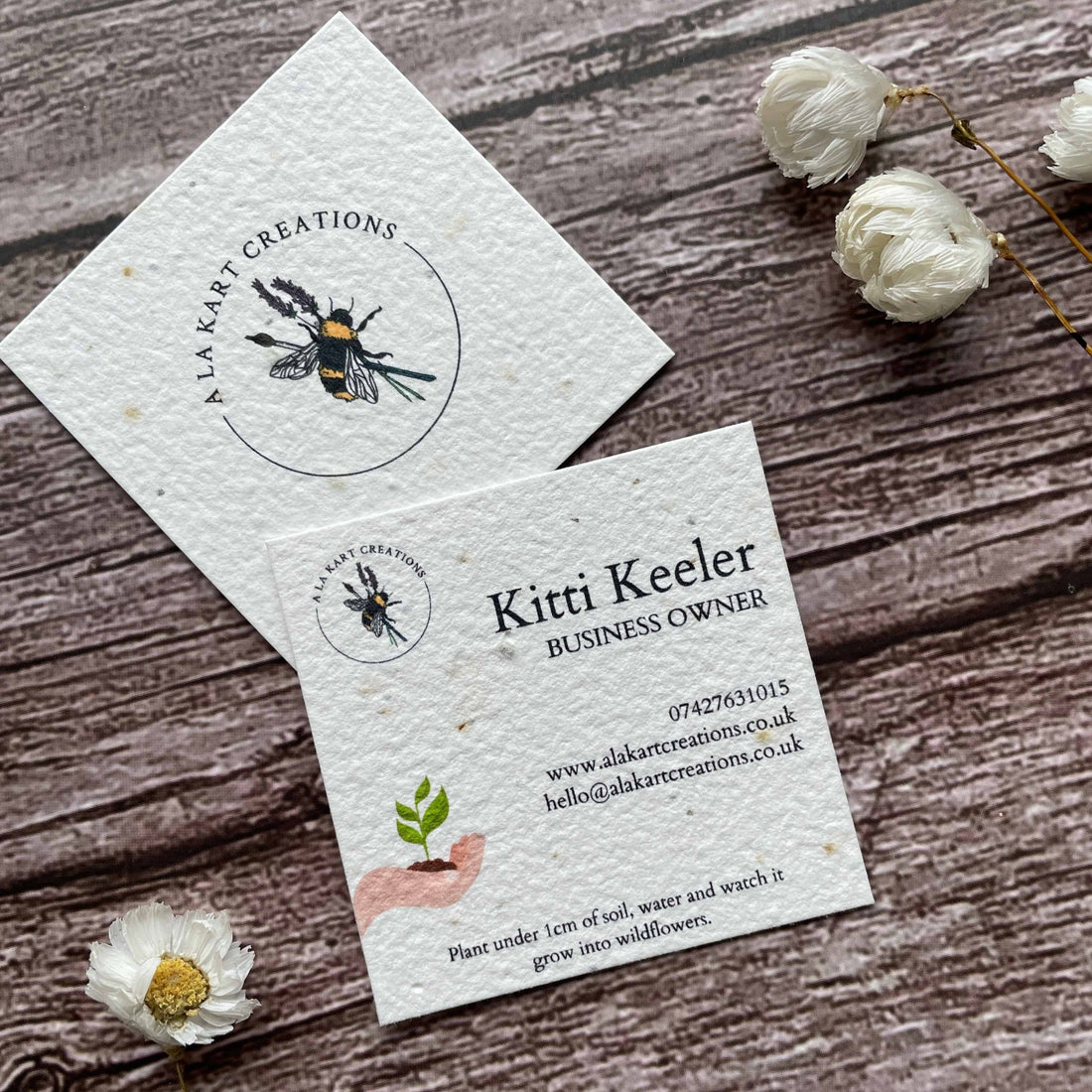 square plantable seed paper business cards with sustainable future design featuring hand holding growing seedling, angled left, alakartcreations