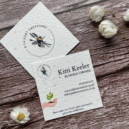 square plantable seed paper business cards with sustainable future design featuring hand holding growing seedling, angled left, alakartcreations