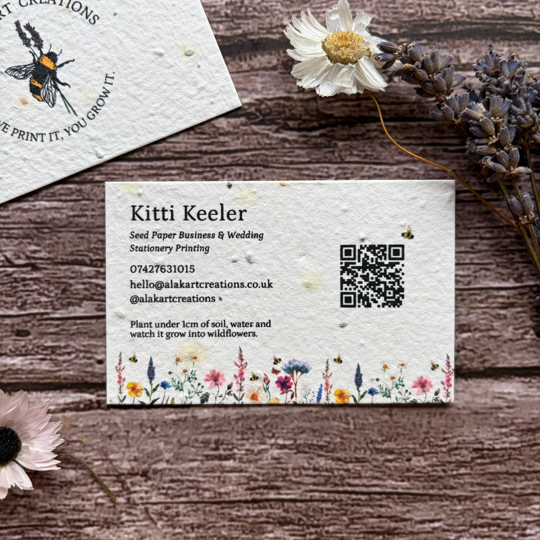 Seed paper business cards with floral design and QR code on a wooden surface.