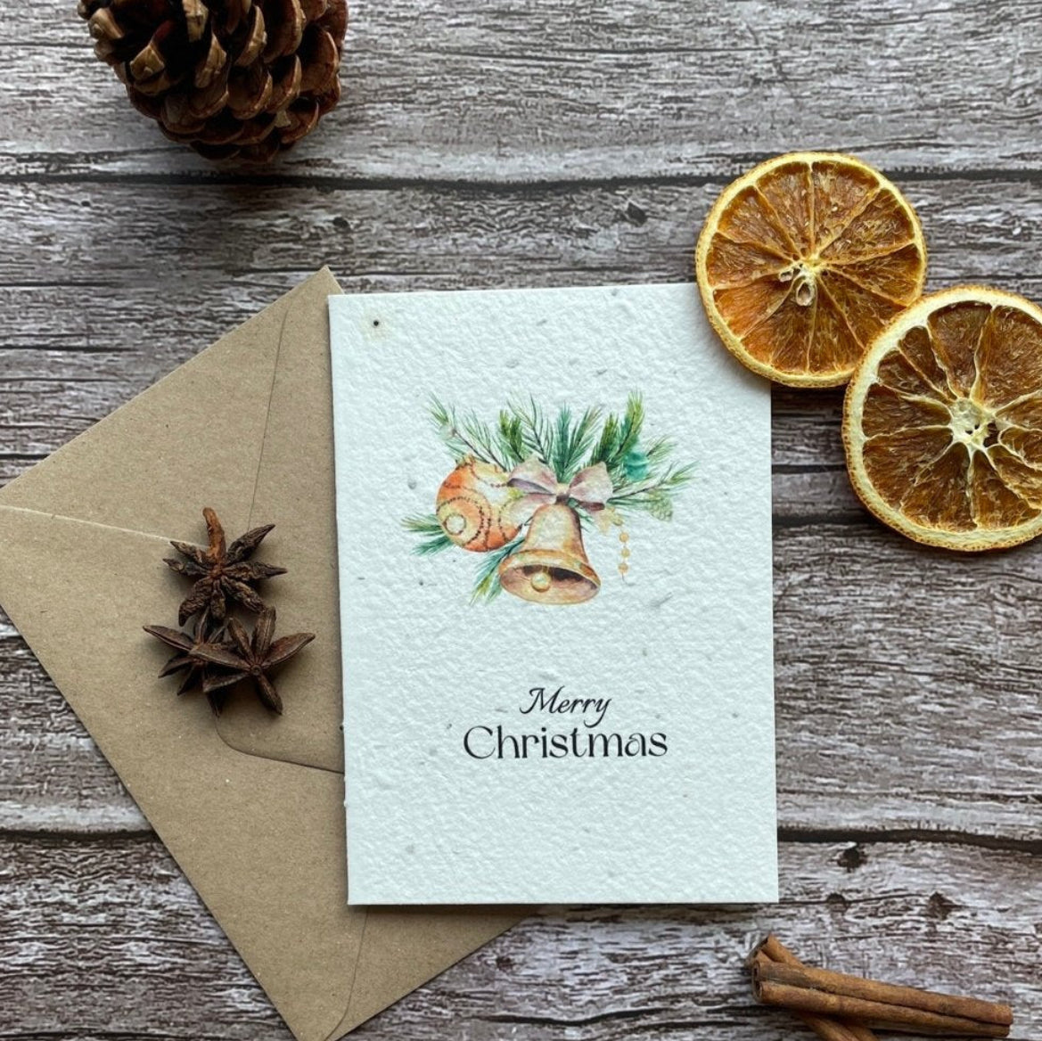 A personalized plantable Christmas card with a design of a golden bell tree, accompanied by an envelope and two whole lemons on a wooden surface.