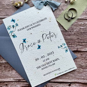 personalised plantable wedding invitations in dusty blue theme, showing angled view with colour matched envelope, floral design on wooden background