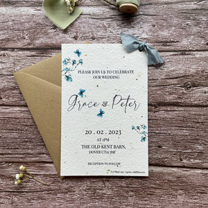 personalised plantable wedding invitations dusty blue theme, front view with eco-friendly brown kraft envelope, floral design on wooden background