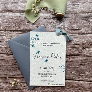 personalised plantable wedding invitations in dusty blue theme, showing front view with colour matched envelope, floral design on wooden background