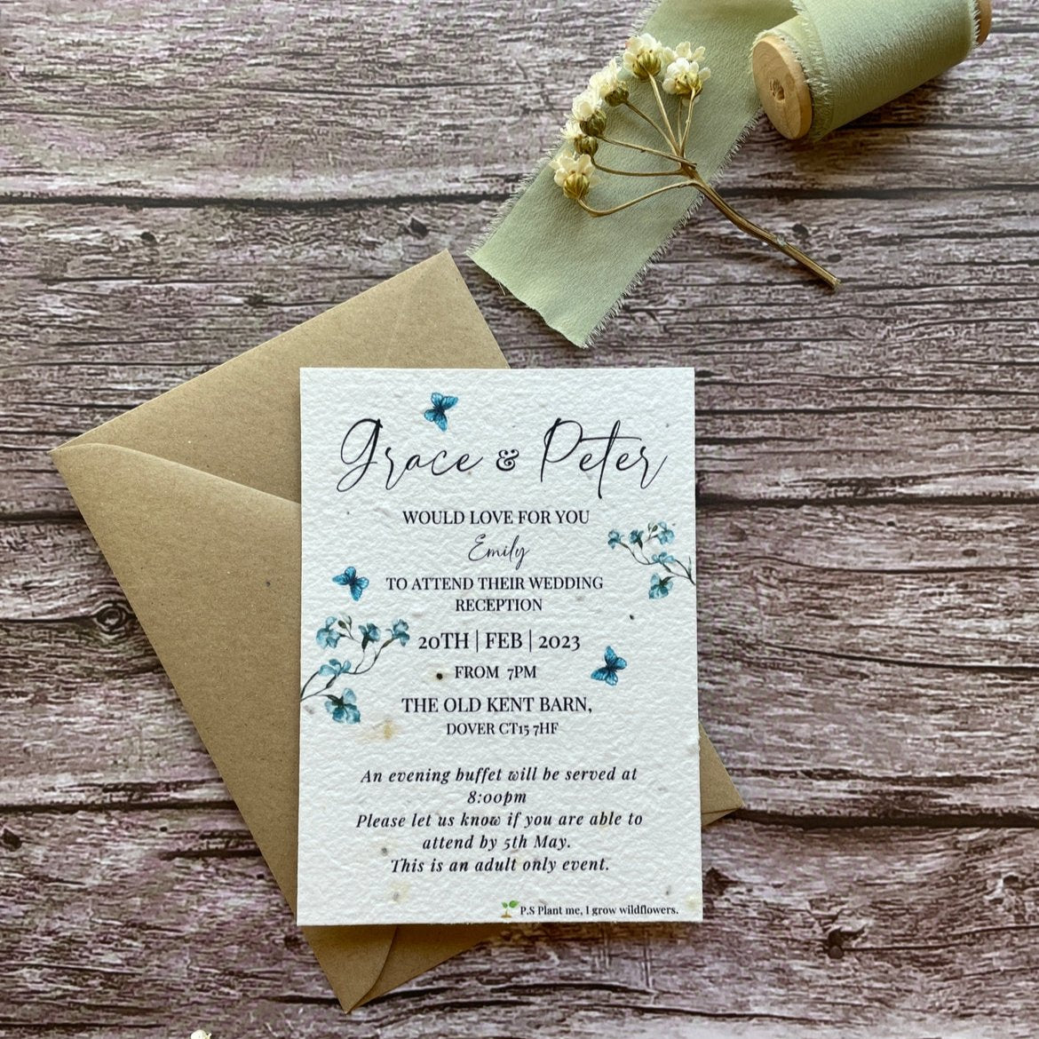 plantable evening guest wedding invitations dusty blue theme, front view with eco-friendly brown kraft envelope, floral design on wooden background