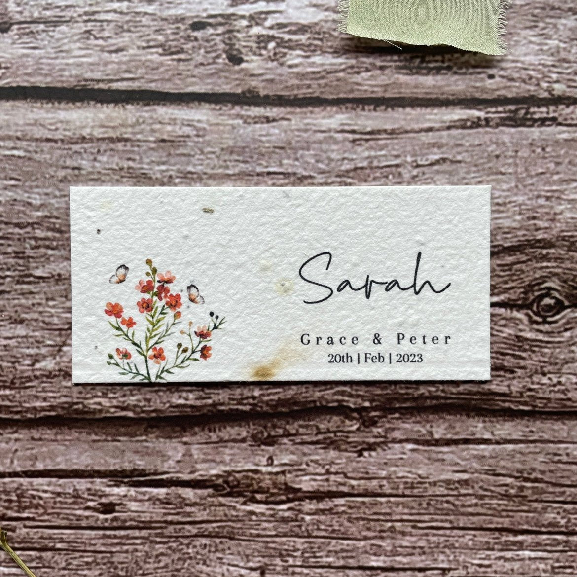 plantable seed paper wedding guest place cards in burnt orange theme, showing a close-up front view, floral design on wooden background.