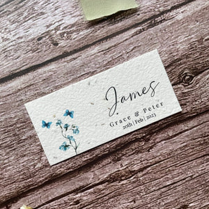 plantable seed paper wedding guest place cards in dusty blue theme, showing an angled view, floral design on wooden background, eco-friendly