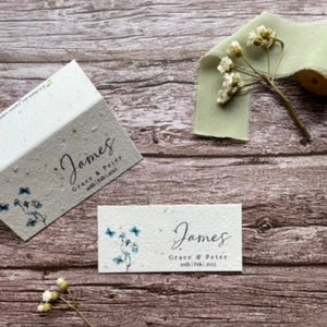 plantable seed paper wedding guest place cards in dusty blue theme, showing flat and standing views, floral design on wooden background, eco-friendly