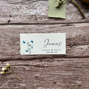 plantable seed paper wedding guest place cards in dusty blue theme, showing a close-up front view, floral design on wooden background, eco-friendly