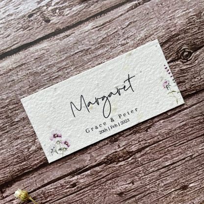 plantable seed paper wedding guest place cards in lilac theme, showing an angled view, floral design on wooden background, eco-friendly