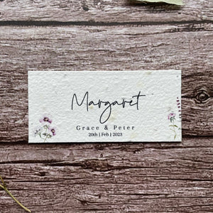 plantable seed paper wedding guest place cards in lilac theme, showing a close-up front view, floral design on wooden background, eco-friendly