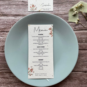 plantable seed paper wedding menu card in burnt orange theme, placed on a blue plate, floral design on wooden background, eco-friendly