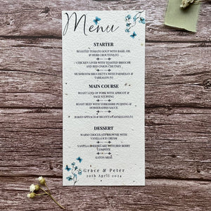 plantable seed paper wedding menu card in dusty blue theme, showing a close-up front view, floral design on wooden background, eco-friendly