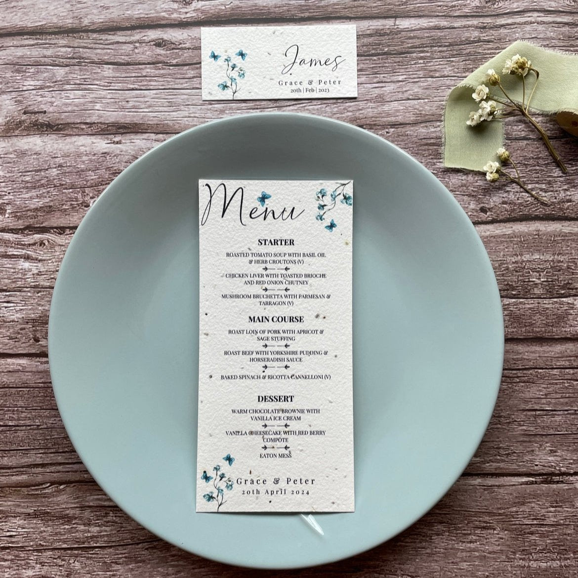 plantable seed paper wedding menu card in dusty blue theme, placed on a blue plate, floral design on wooden background, eco-friendly