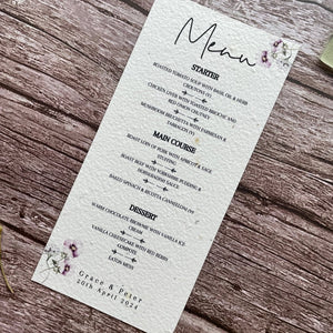 plantable seed paper wedding menu card in lilac theme, showing an angled view, floral design on wooden background, eco-friendly