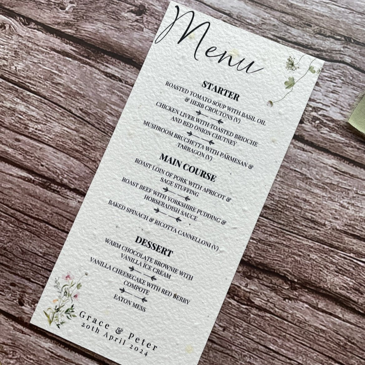 plantable seed paper wedding menu card in spring green theme, showing an angled view, floral design on wooden background, eco-friendly