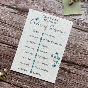 plantable seed paper wedding order of service card in dusty blue theme, showing angled right view, floral design on wooden background, eco-friendly