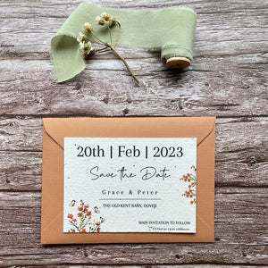 plantable seed paper wedding save the date card in burnt orange theme, shown with theme colour matched envelope, floral design on wooden background.