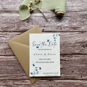 plantable seed paper wedding save the date card in dusty blue theme, shown with eco-friendly brown kraft envelope, floral design on wooden background, eco-friendly