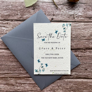 plantable seed paper wedding save the date card in dusty blue theme, shown with theme colour matched envelope, floral design on wooden background, eco-friendly