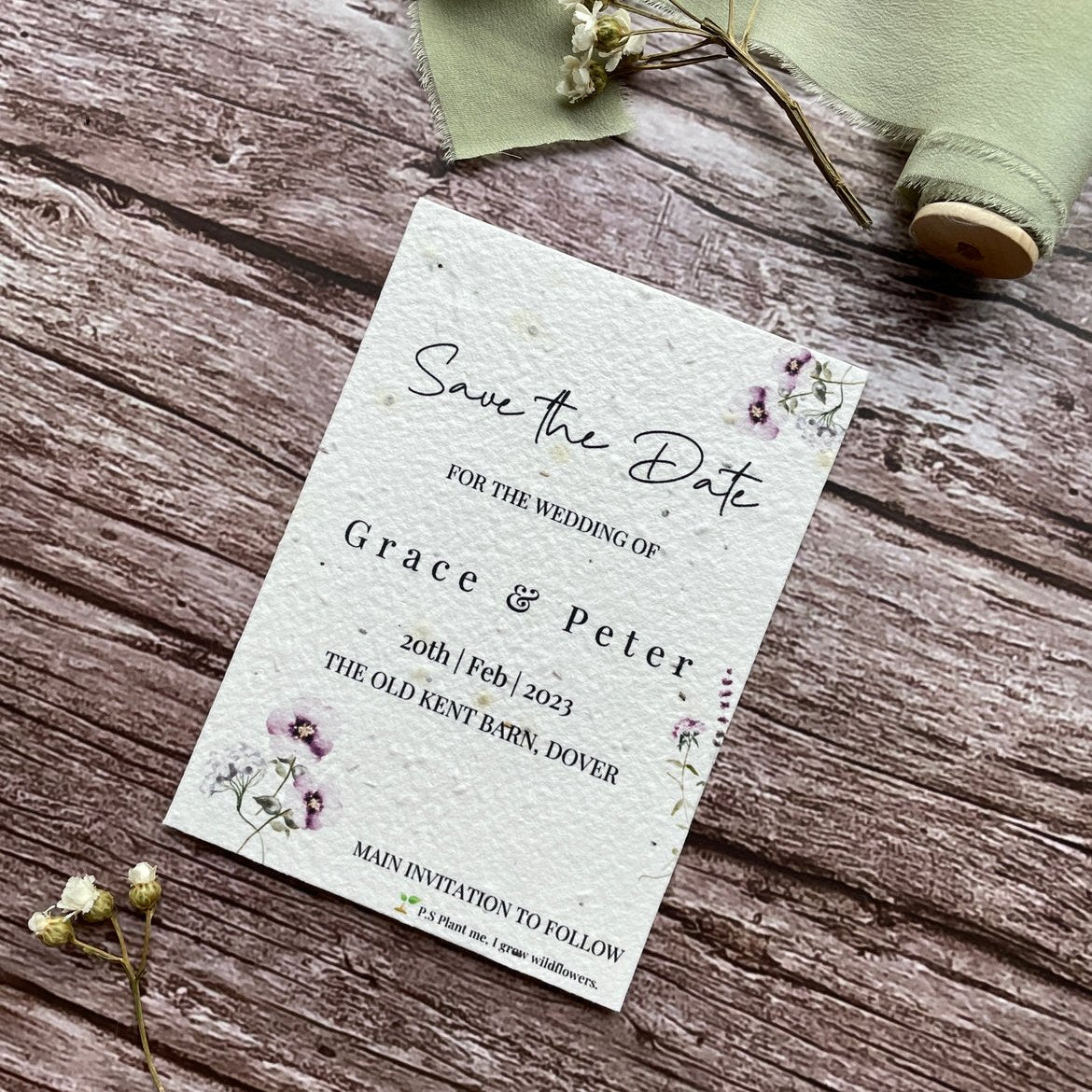 plantable seed paper wedding save the date card in lilac theme, showing angled view, floral design on wooden background, eco-friendly