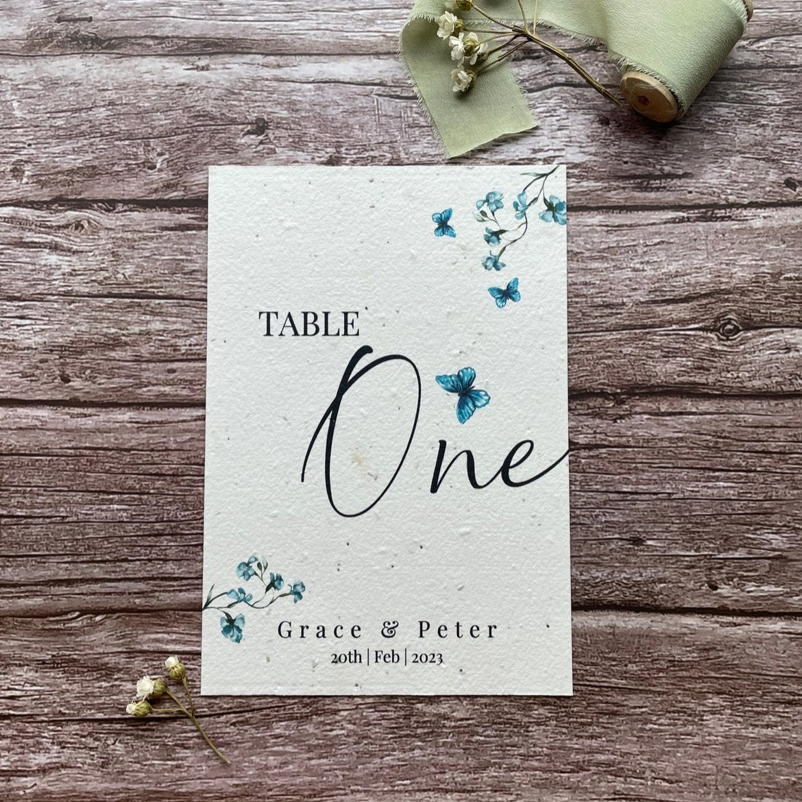 plantable seed paper wedding table number/name card with blue sweet peas and butterflies, showing front view, floral design on wooden background