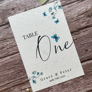 plantable seed paper wedding table number/name card in dusty blue theme, showing angled left view, floral design on wooden background, eco-friendly