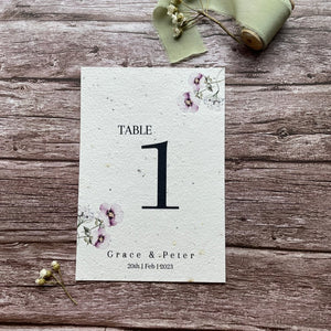 plantable seed paper wedding table number/name card in lilac theme, showing front view, floral design on wooden background, eco-friendly