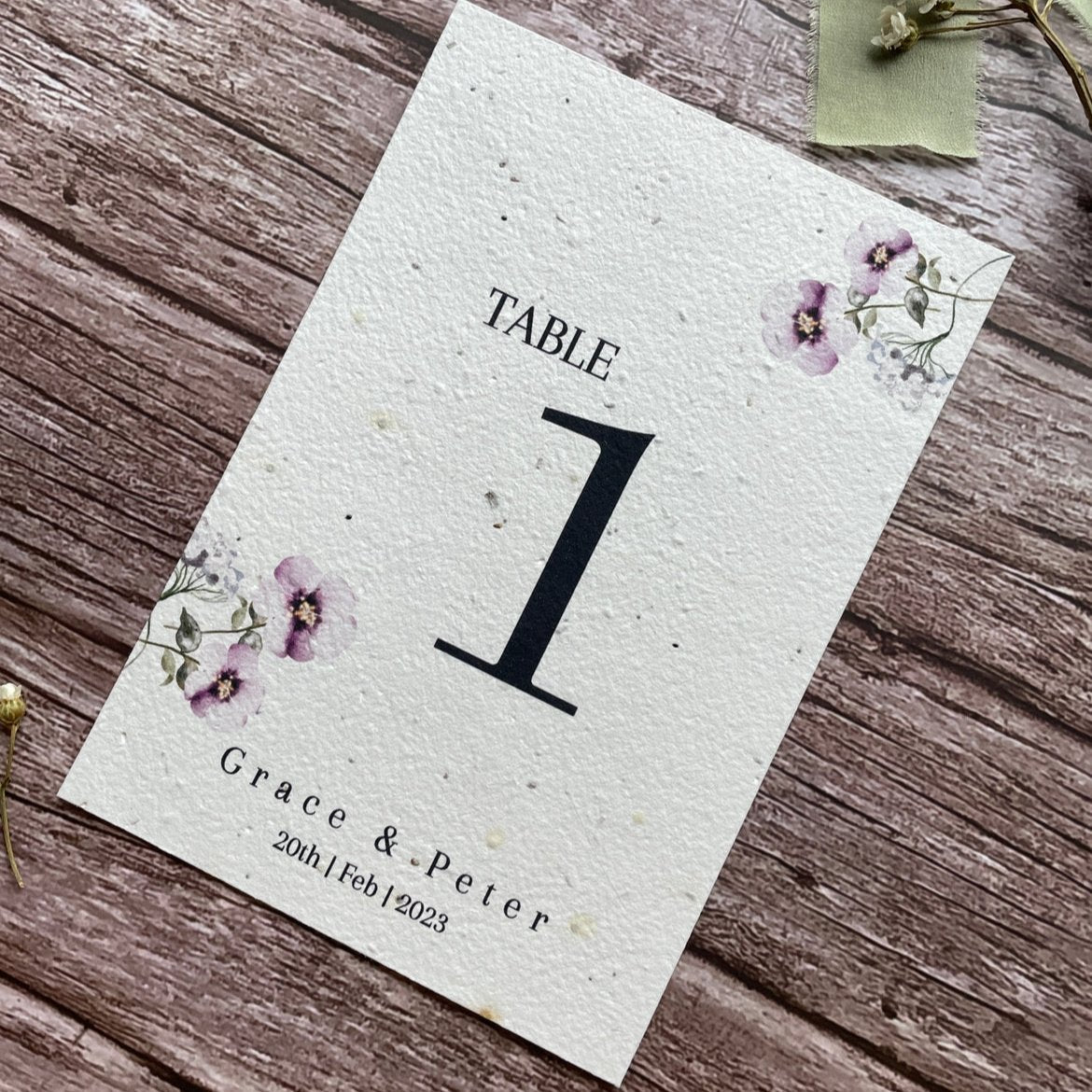 plantable seed paper wedding table number or name cards in lilac theme, angled view with floral design on wooden background, eco-friendly, alakartcreations
