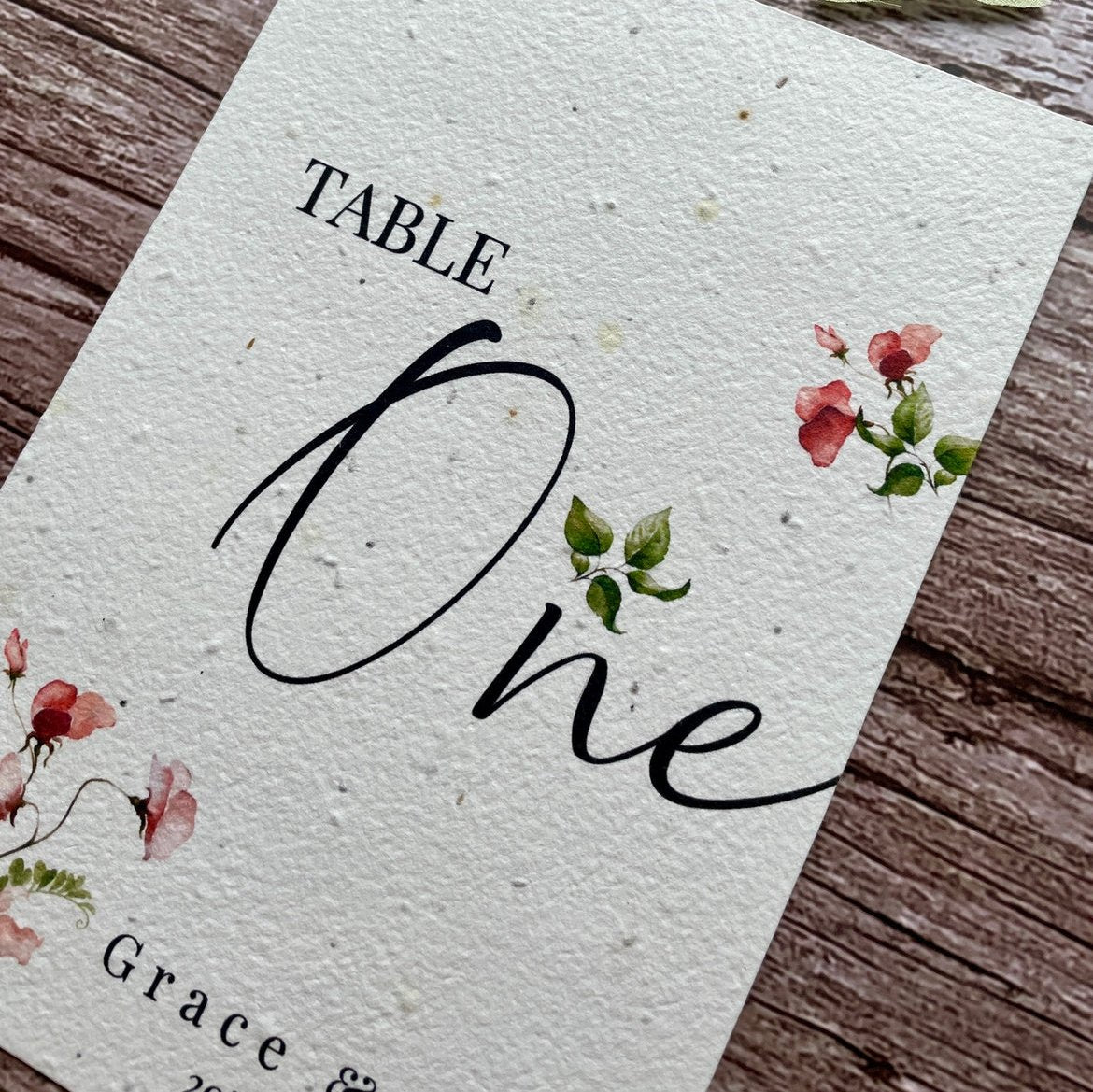 plantable seed paper wedding table number or name cards in sweet pea theme, close-up angled view with floral design on wooden background, eco-friendly, alakartcreations