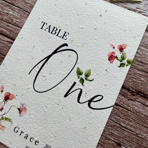 plantable seed paper wedding table number or name cards in sweet pea theme, close-up angled view with floral design on wooden background, eco-friendly, alakartcreations