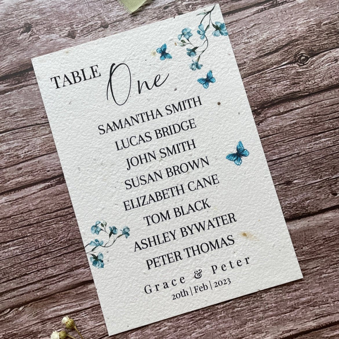 plantable seed paper wedding table seating plan with blue sweet peas, angled left view with floral design on wooden background