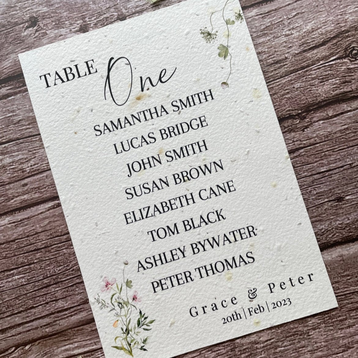 plantable seed paper wedding table seating plan in spring green theme, showing angled left view, floral design on wooden background, eco-friendly