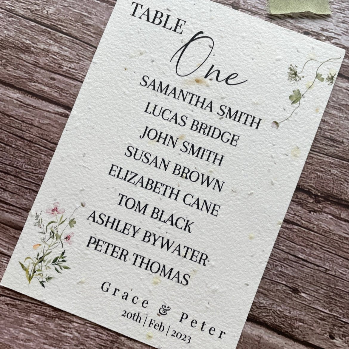 plantable seed paper wedding table seating plan in spring green theme, showing angled right view, floral design on wooden background, eco-friendly